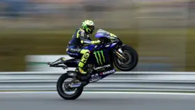 Valentino Rossi levanta la rueda trasera de su Yamaha en plena carrera, con su icónico casco amarillo y traje azul.