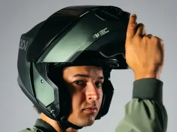 Hombre ajustando su casco integral o modular, de color verde militar, con sistema de ventilación.