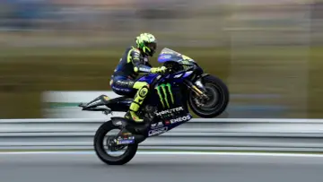 Valentino Rossi levanta la rueda trasera de su Yamaha en plena carrera, con su icónico casco amarillo y traje azul.