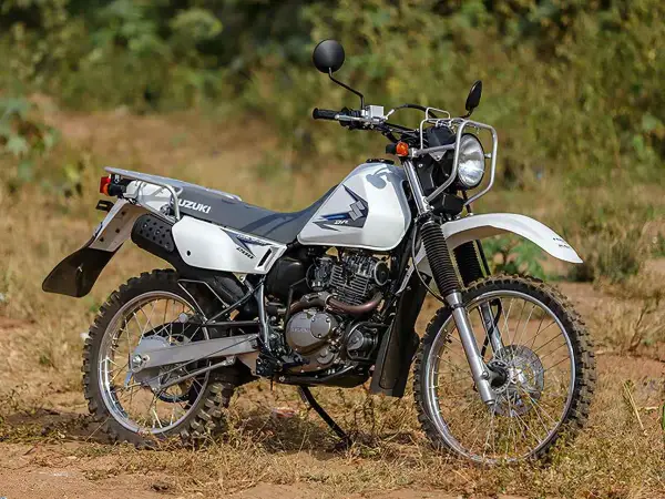 Suzuki DR 200 lista para la aventura. Moto blanca de doble propósito con neumáticos todoterreno, lista para explorar caminos rurales.