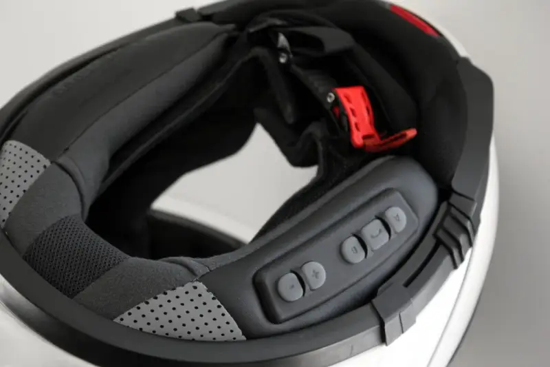 Detalle del interior de un casco modular, mostrando el proceso para instalar intercomunicador. Botones de control visibles.