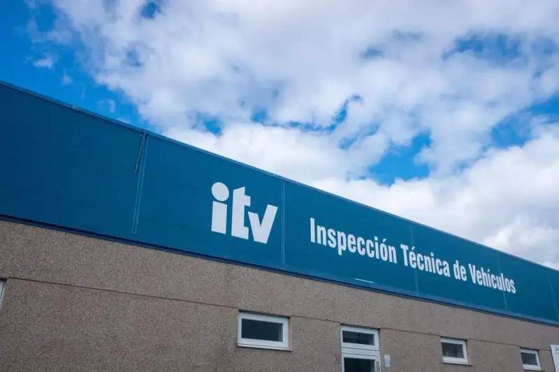 Edificio de la ITV bajo un cielo azul con nubes. El letrero blanco dice "itv Inspección Técnica de Vehículos".