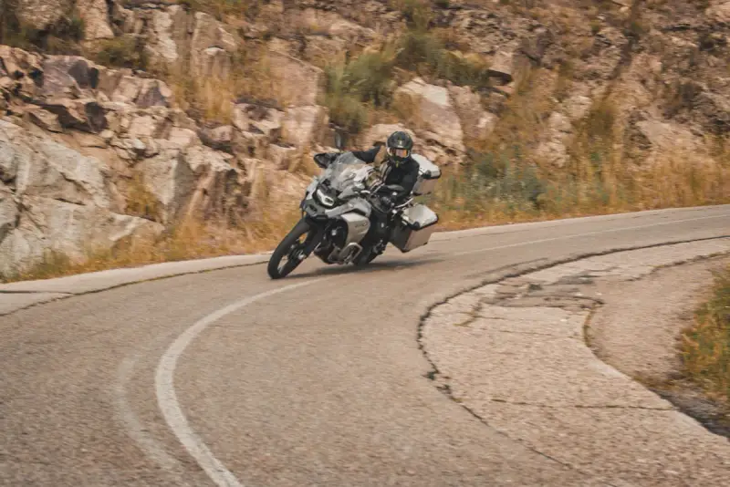 Motociclista en pruebas de motos, inclinado en una curva de carretera montañosa.