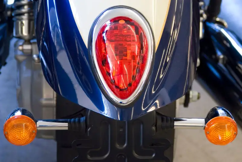 Detalle de la parte trasera de una moto azul y blanca, con intermitentes naranjas y luz roja. Podría ser una multa por llevar luces led moto.